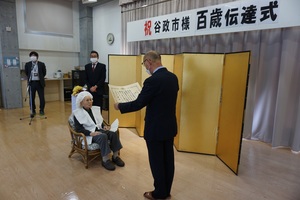 谷 政市さんに100歳のお祝いと記念の品をお渡ししている様子