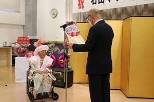 石山マサノさんに100歳のお祝いを述べている様子